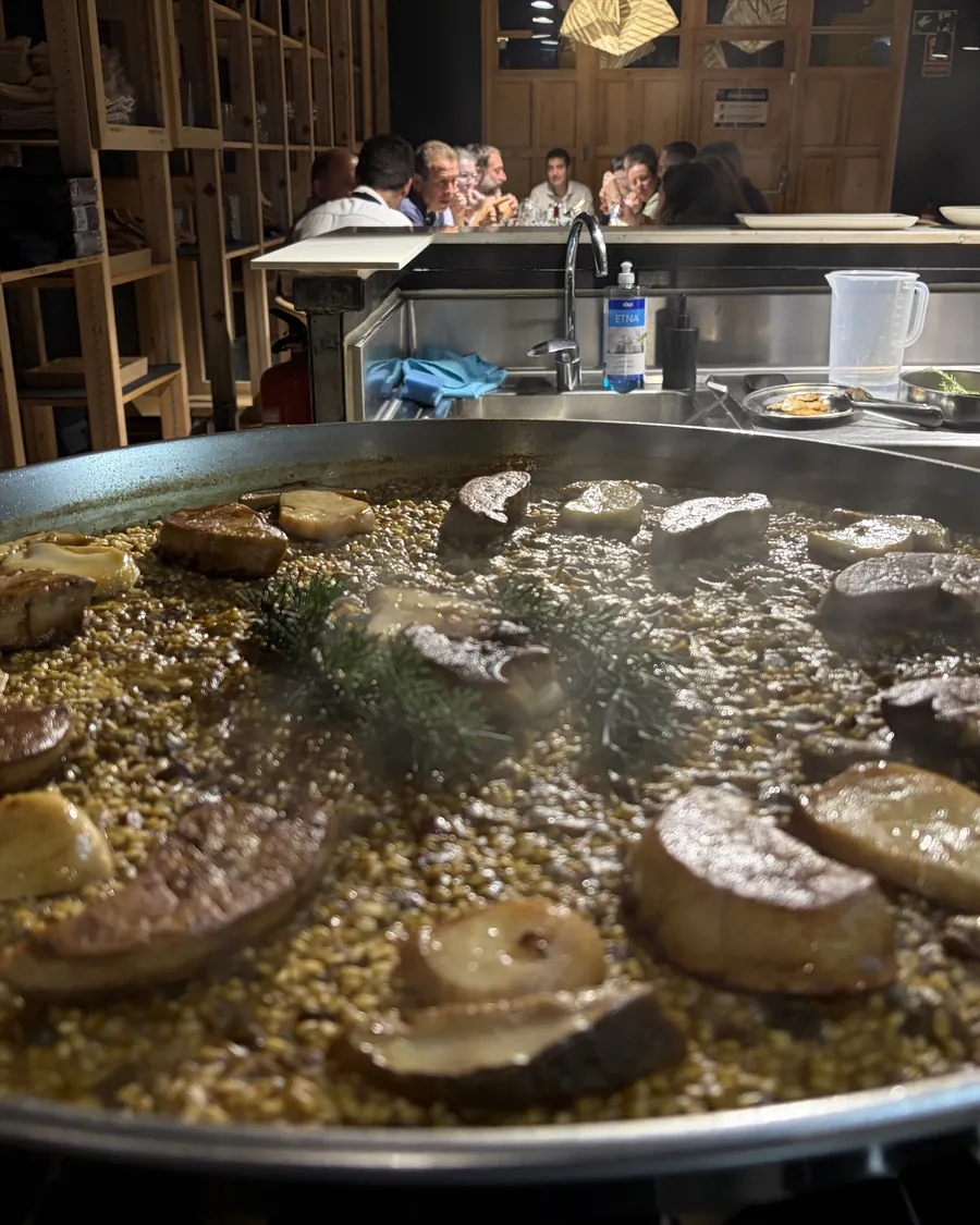 Paella de arroz con setas y foie recién hecha en la cocina, con los invitados cenando al fondo